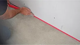 A contractor places joint tape between a wall and the floor
